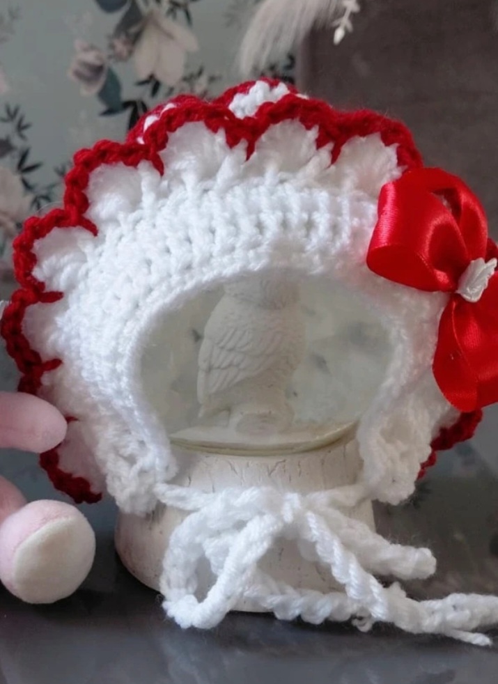 Handmade baby girls bonnet in white edged in red.