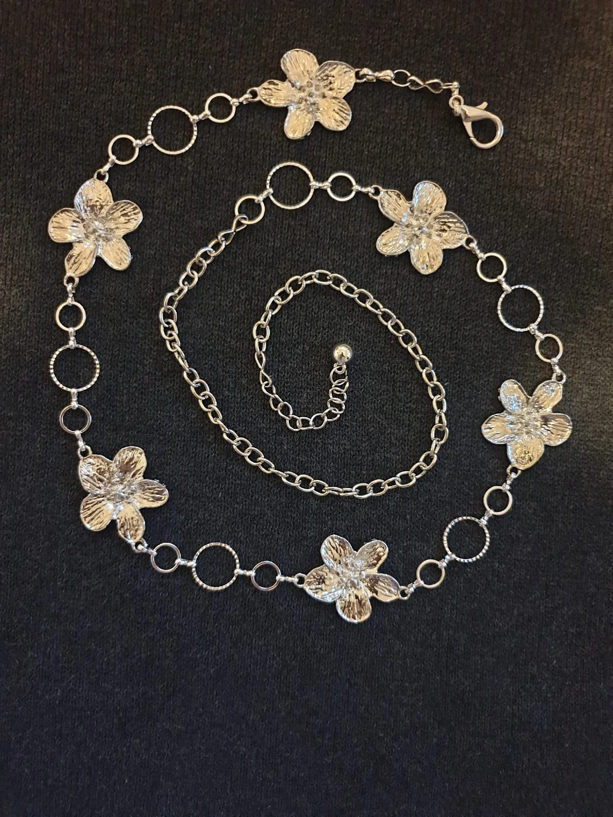 Silver-toned flower adjustable chain belt with five silver flower charms and circular links.