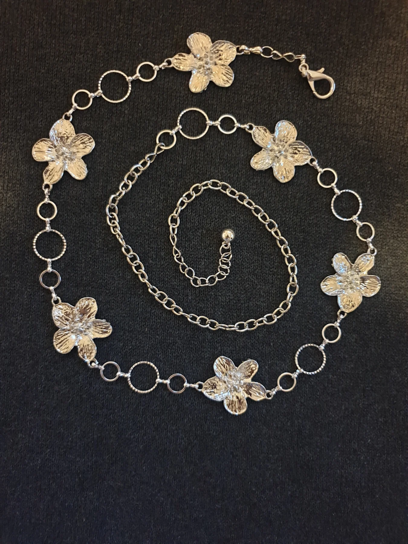 Silver-toned flower adjustable chain belt with five silver flower charms and circular links.