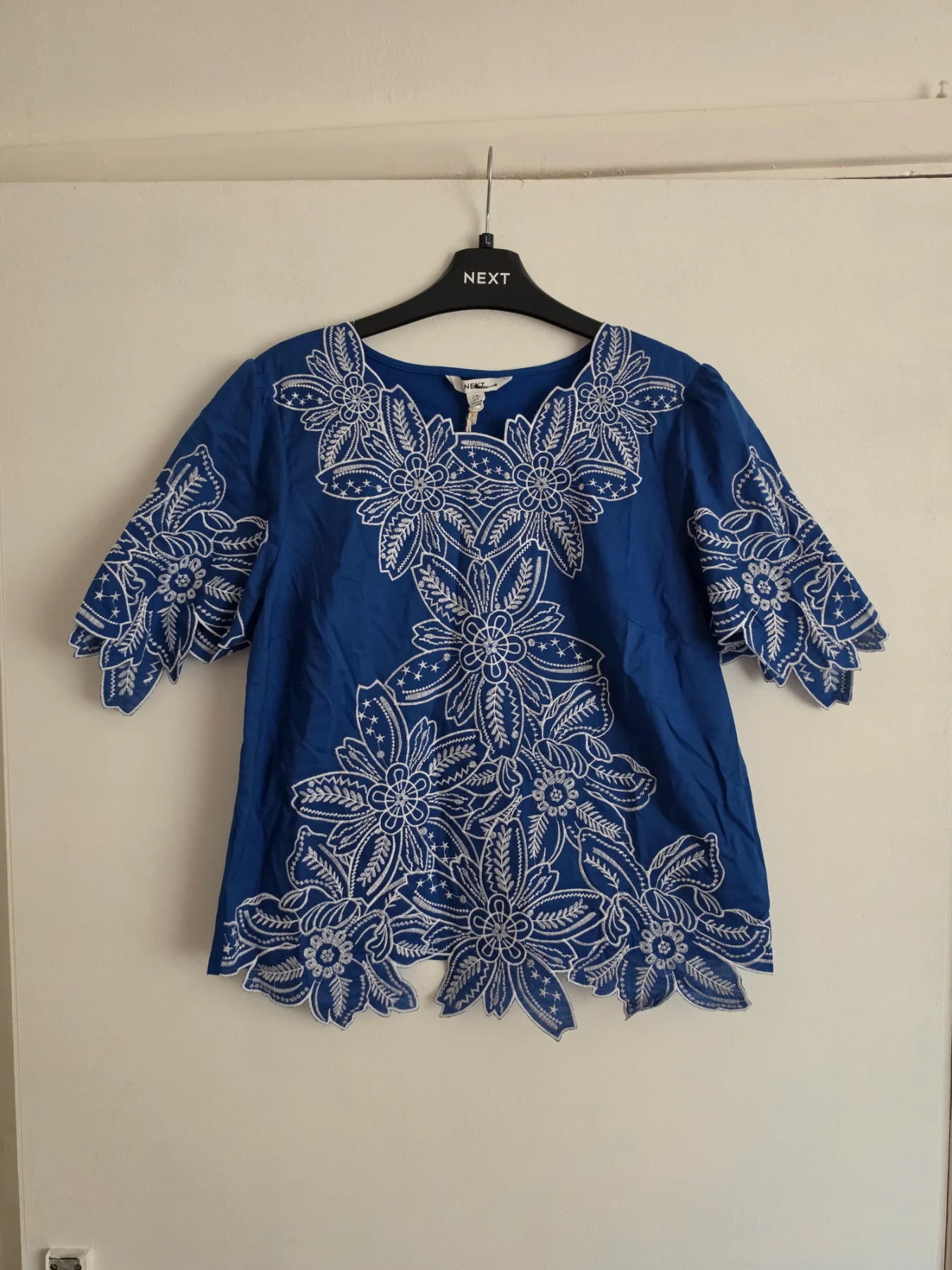 Blouse with floral embroidery and a decorative cut-out hem.