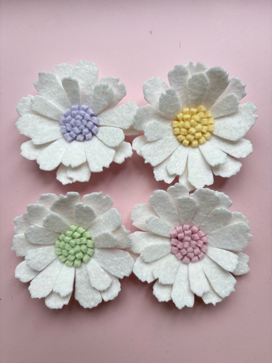 Four felt daisies with pastel centres.